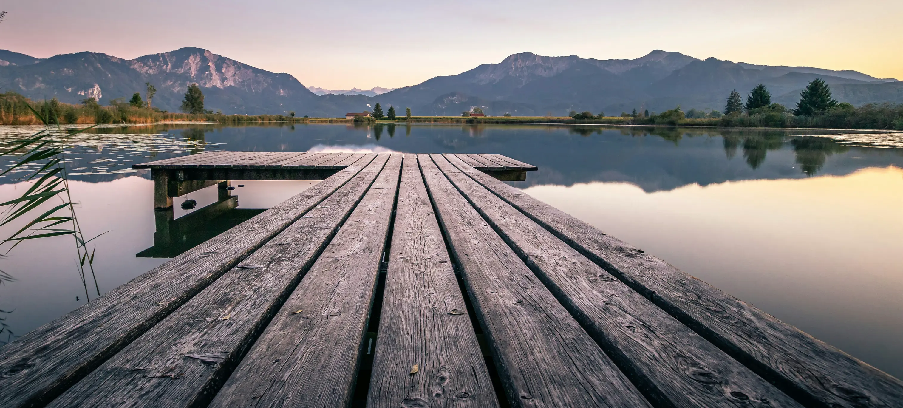 Holzsteg an einem See mit Bergen im Hintergrund bei Dämmerung